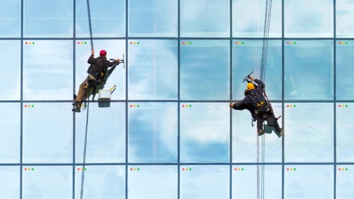 two window washers scaling the side of a building with all glass windows. each panel of glass looks like a Mac window with the red, yellow, and green buttons in the top left of each pane.