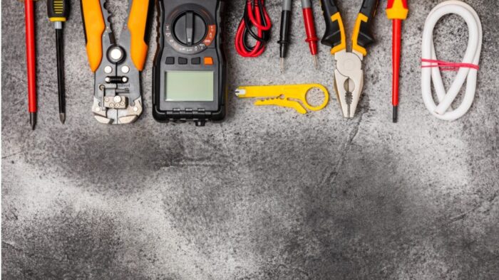 a row of electrical tools across the top of the image on a gray background. among the tools are pliers, wire crimper, screwdriver, and multimeter