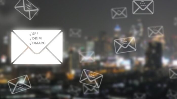 Blurred image of a city at night. In the foreground, drawings of the back of envelopes, one main one white, the others are white outlines of the envelopes with the background of the image showing through. On each envelope is the text ✔️SPF ✔️DKIM ✔️DMARC