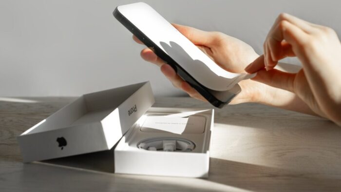 a person is peeling the protective cover off of a new iPhone. the box is on the table below