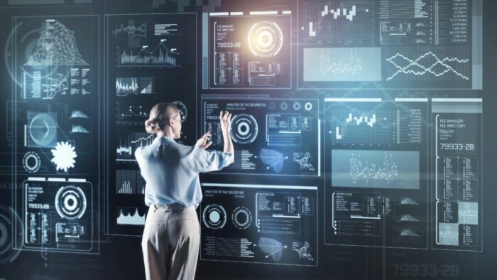 back view of a woman in front of a large wall of virtual screens and controls. she is using her hands in the air to control the screens.