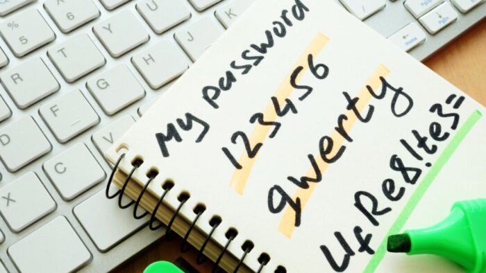 picture of a notebook on top of a keyboard. writing on notebook says "my password" and then has several very insecure passwords. green highlighter resting at the bottom of the notebook.