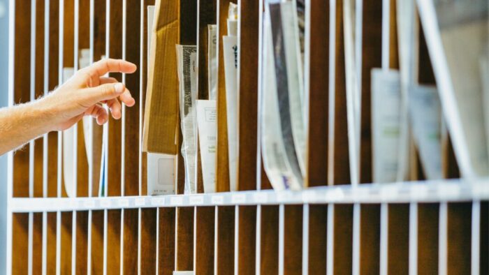 a wall of physical inbox slots filled with papers. A hand reaches in from the left to get papers out of one of the slots.