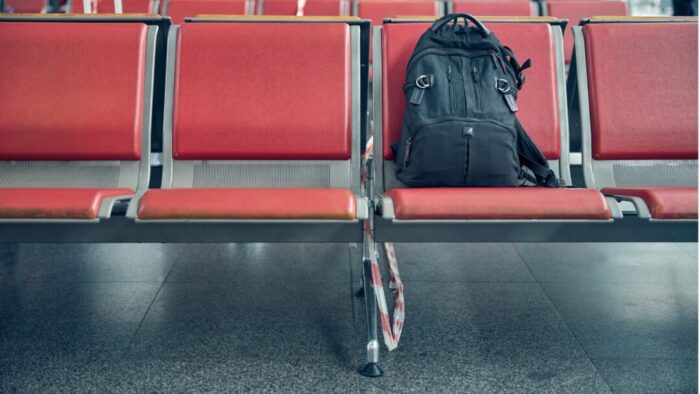 a lonely black backpack sits on the front row of several rows of red airport gate chairs.