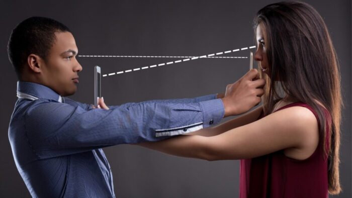 two people facing each other and overlapping their arms with their phones outstretched and in front of the other person's face. digital overlay of two dashed lines, one for each person going from their eyes to their own phone.