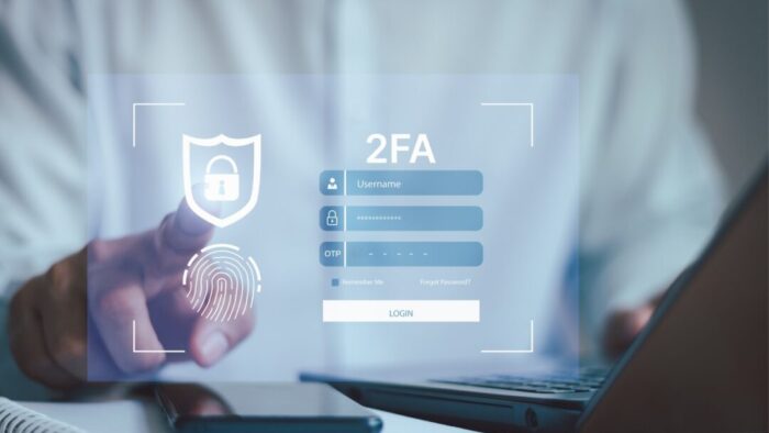 blurry picture of the torso of a person wearing a white shirt with an index finger extended as if to look like it's about to tap the phone screen below it. digital overlay of a login screen with "2FA" at the top.