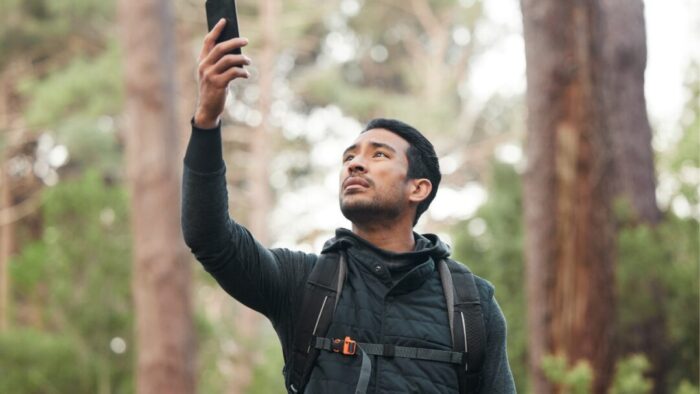a guy holding his phone up to the sky while standing in a forest.