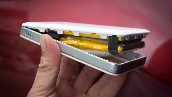 a hand holding up a broken open power bank. the power bank is open because of battery swelling. reddish background.