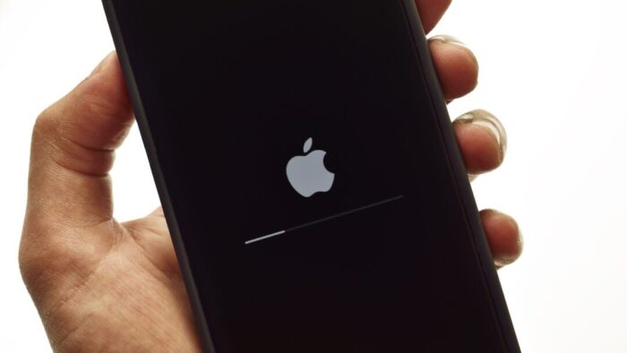 a disembodied hand against a white background holds an iPhone that is updating