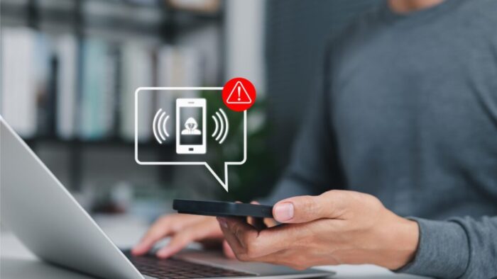 blurred image of a person holding an iPhone with one hand and typing on a laptop with the other. overlaid image represents an alert coming from the phone.