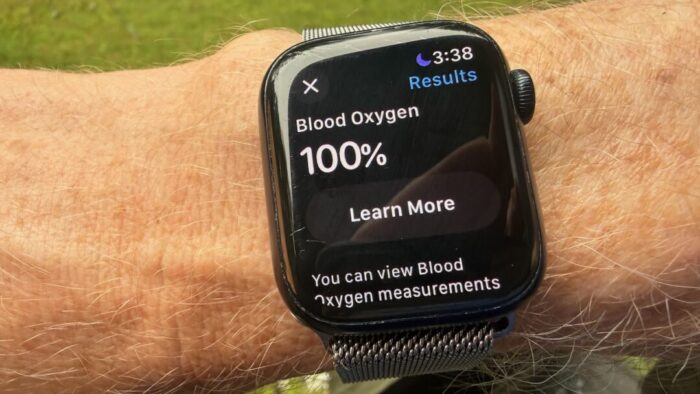 Apple Watch on a hairy right wrist shows the blood oxygen screen. The person wearing the watch has a 100% blood oxygen level.