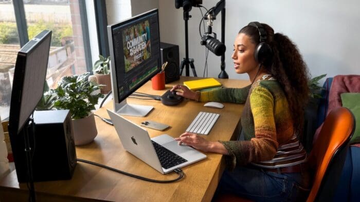 Black woman with long curly hair sitting at her desk. Looks like a podcast studio set up.