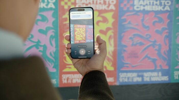 event posters (like concert posters) in the background. in the foreground, a person holding out a phone taking a picture of one of the posters to use it for Visual Intelligence