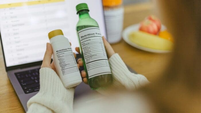 two hands holding one bottle each. the bottles are rotated so that their nutrition labels are what the person holding them is looking at