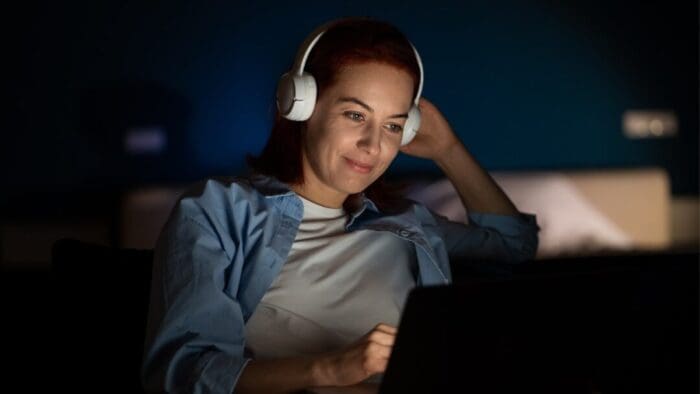 woman in a dark room wearing over the ear headphones while watching something on her computer screen