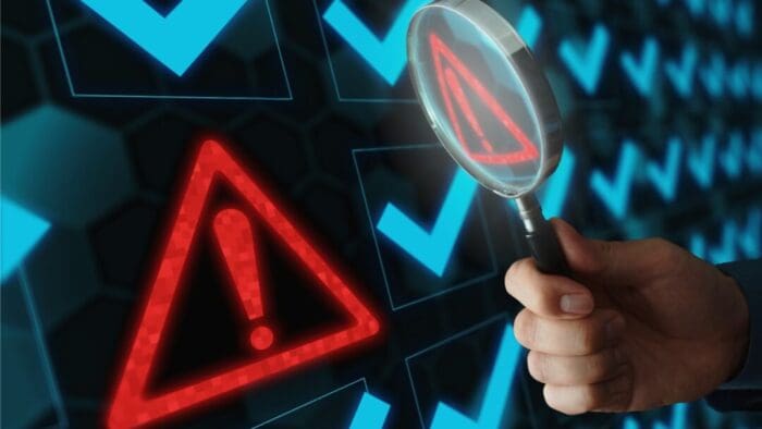 hand holding a magnifying glass in front of a screen full of blue checkmarks and one red alert box.