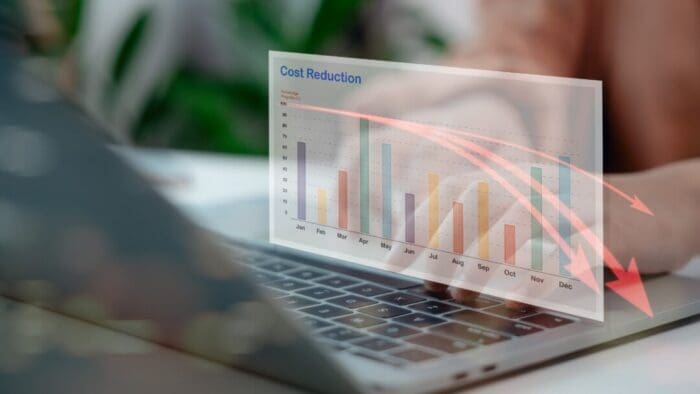 Blurred pic of an open laptop with someone's hands typing on it. Translucent overlay of a bar chart measuring something by month with red arrows arcing downward off the December edge of the chart.