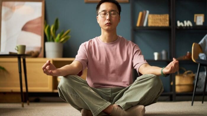 man in pink shirt and green pants sitting on the floor in a criss cross position. his hands are resting on his knees, facing upward.
