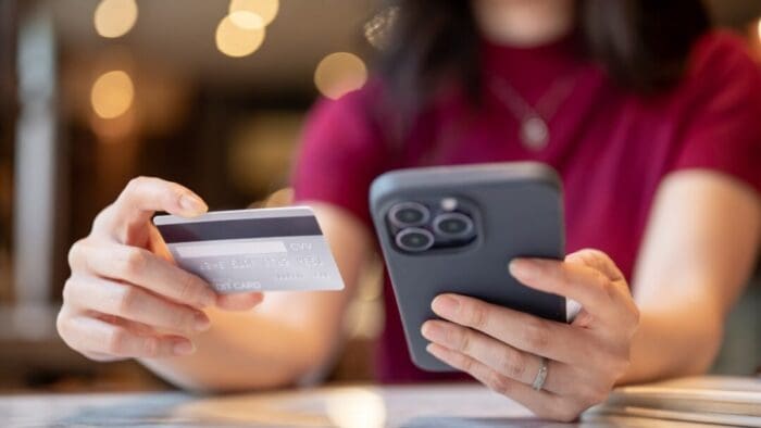 woman in a red shirt holding her iPhone in one hand and her credit card in the other