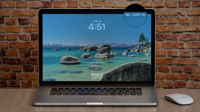 MacBook Pro open on a table against a brick wall. the top right of the screen has a magnifier drawn over it highlighting the keyboard input source