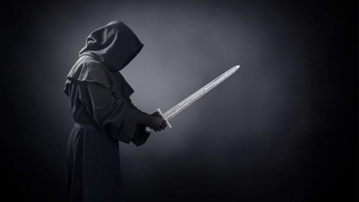 black and white photo of the side view of a hooded person holding a sword