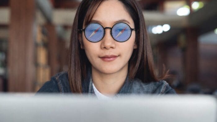 A woman with straight dark hair is wearing round glasses. the lenses are Safari compass icons.