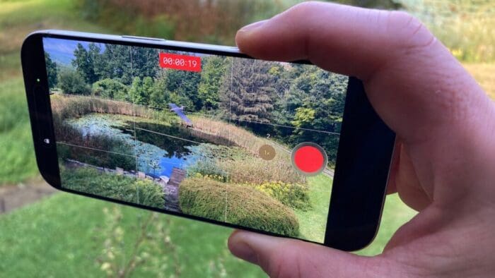 disembodied hand holding an iPhone taking a picture of a heron over a pond
